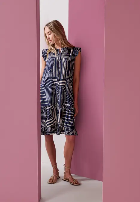 Frau in blau-weiß gemustertem Kleid vor rosa Wänden.