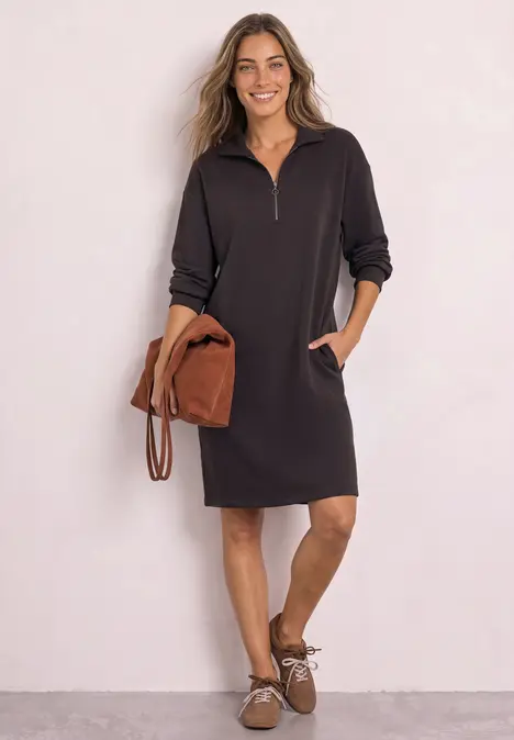 Frau in schwarzem Sweatkleid mit halbem Reißverschluss, Taschen und braunen Accessoires.