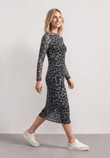 Eine Frau in seitlicher Pose trägt ein knielanges, langärmeliges, gemustertes Kleid und weiße Sneaker.