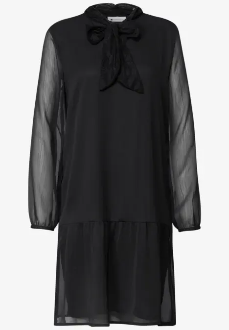 Robe noire en chiffon jusqu’aux genoux, manches transparentes, volants au bas et col noué.