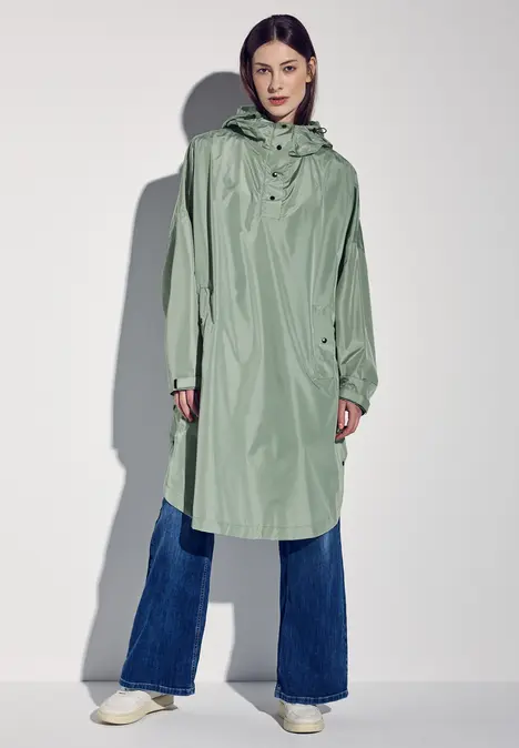 Frau trägt mintgrünen Regenmantel, blaue Jeans und weiße Schuhe.