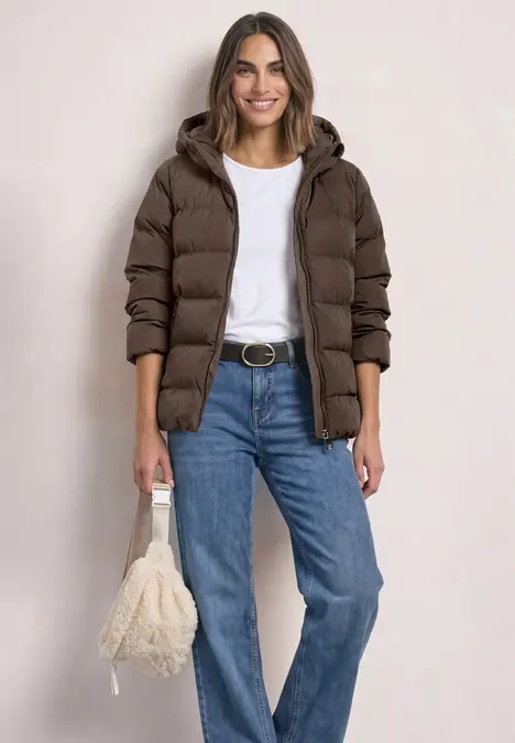 Femme portant un manteau matelassé marron, un t-shirt blanc, un jean bleu et un sac pelucheux.