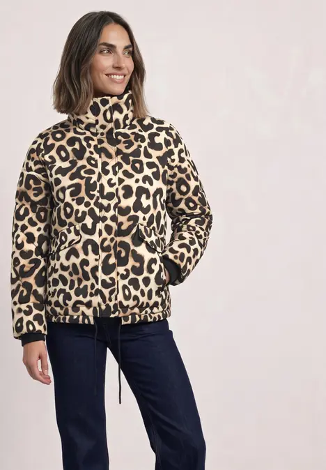 Frau in beige-schwarz gemusterter Leopardenjacke mit hohem Kragen, Kordelzug und Taschen, kombiniert mit blauen Jeans.