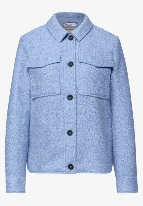 Hellblaue Wolljacke mit Hemdkragen, schwarzen Knöpfen und zwei aufgesetzten Brusttaschen.
