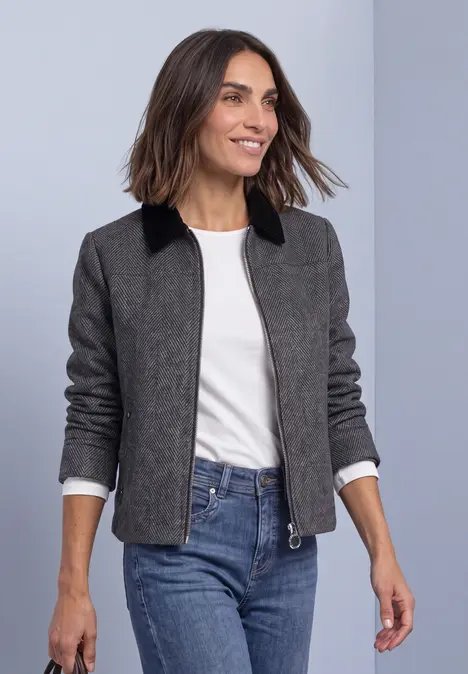 Femme souriante en veste grise à col noir, t-shirt blanc et jean bleu, marchant.