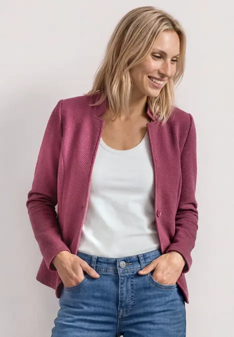 Frau mit rosa Cardigan und weißem Top, steht lächelnd, Hände in Jeans-Taschen