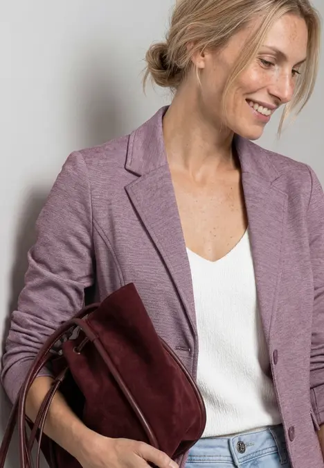 Eine Person mit unkenntlichem Gesicht trägt einen fliederfarbenen Blazer, eine weiße Bluse und eine weinrote Tasche.