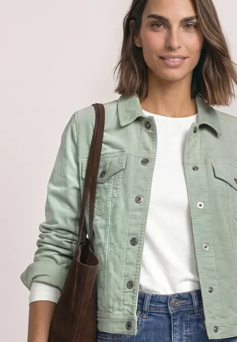 Junge Frau in grüner Jeansjacke, weißem T-Shirt und Jeans trägt eine braune Umhängetasche.