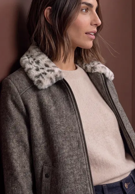 Frau trägt braunen Wollmantel mit geflecktem Kunstfellkragen und hellbeigen Pullover.