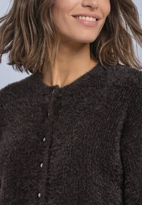 Vrouw met halflang bruin haar, glimlachend, in een donzige bruine cardigan.
