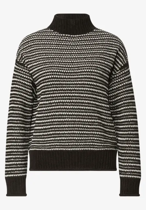 Schwarzer Pullover mit weißem Zickzackmuster, hohem Kragen und gerippten Bündchen.