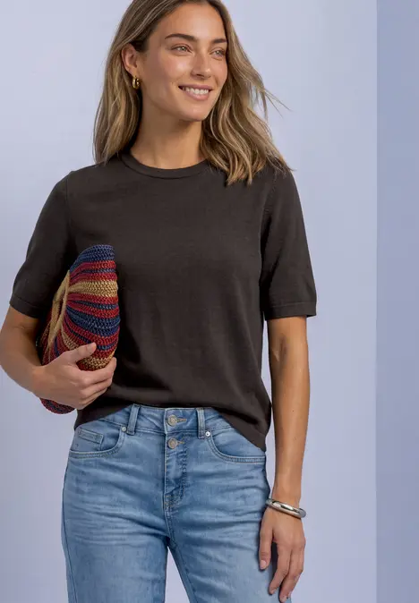 Frau in schwarzem T-Shirt und Jeans hält bunten Hut und lächelt.
