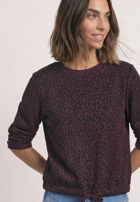 Frau im dunkelvioletten, gemusterten Pullover mit Knoten am Bund, lässig und modern.
