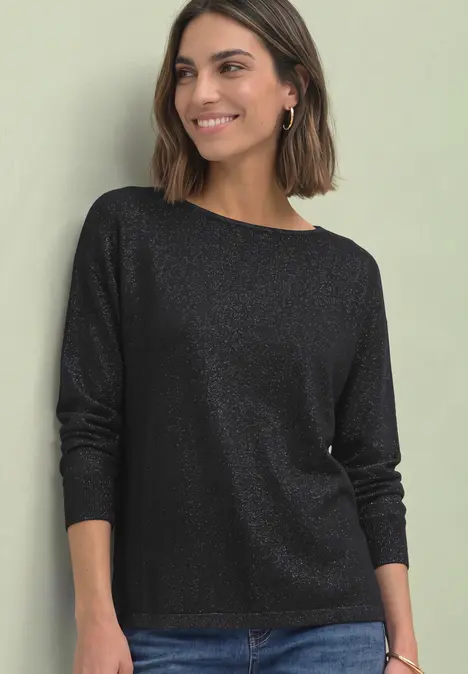 Eine lächelnde Frau trägt ein schwarzes, schimmerndes Langarmshirt vor hellem Hintergrund.
