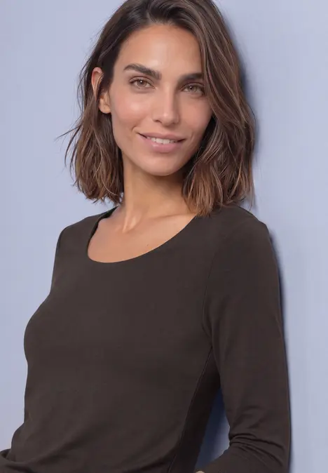 Eine Frau mit schulterlangen braunen Haaren trägt ein langärmeliges braunes Shirt und lächelt dezent.