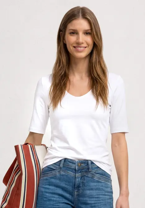 Femme souriante en t-shirt blanc et jean, tenant un sac rayé devant un fond clair