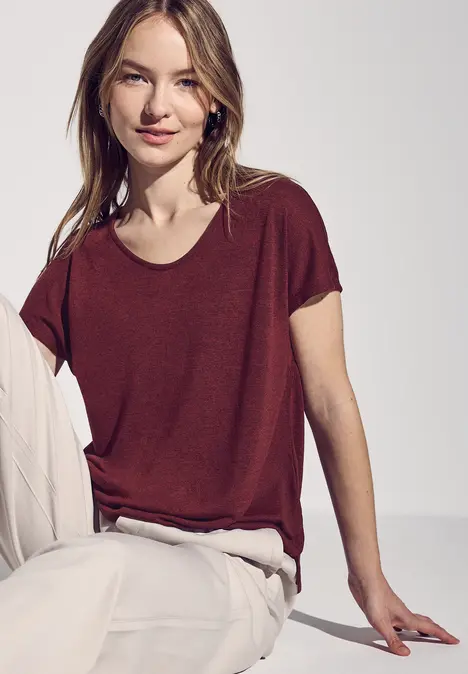 Frau mit bordeauxrotem T-Shirt und heller Hose sitzt entspannt.