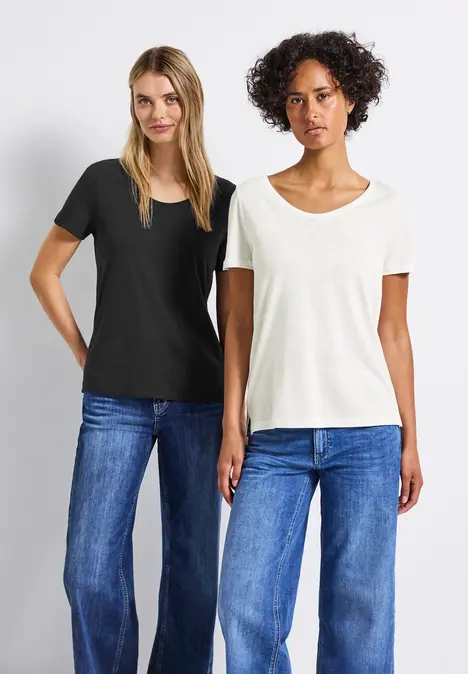 Zwei Frauen in Jeans und T-Shirts posieren nebeneinander vor weißem Hintergrund.