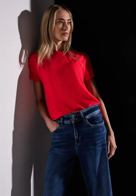 Frau mit rotem T-Shirt und blauer Jeans steht im Licht-Schatten-Kontrast.