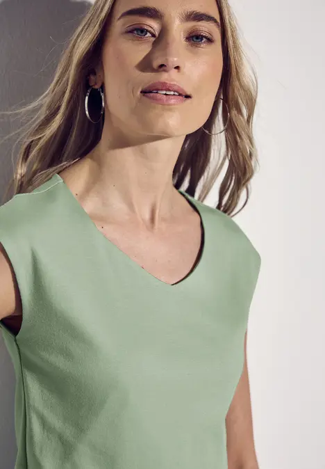 Frau mit langen blonden Haaren, mintgrünem Oberteil und silbernen Creolen.