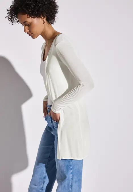 Frau mit weißem Langarmshirt und blauer Jeans im Profil.