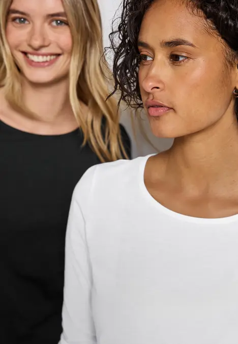 Zwei Frauen in schwarzen und weißen Oberteilen, eine lächelt, die andere schaut ernst.