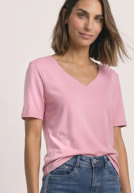 Frau in rosa Kurzarm-Shirt mit V-Ausschnitt kombiniert mit Jeans.