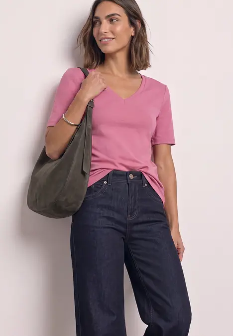 Frau trägt rosa T-Shirt, dunkelblaue Jeans und hält eine olivgrüne Tasche.