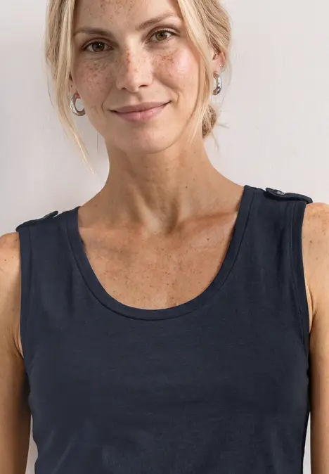 Frau mittleren Alters in schwarzem ärmellosem Top vor weißem Hintergrund.