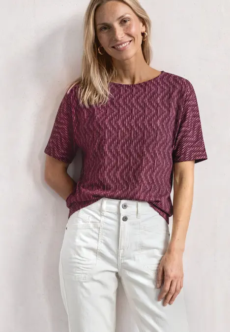 Frau trägt rotes, gemustertes T-Shirt und weiße High-Waist-Jeans