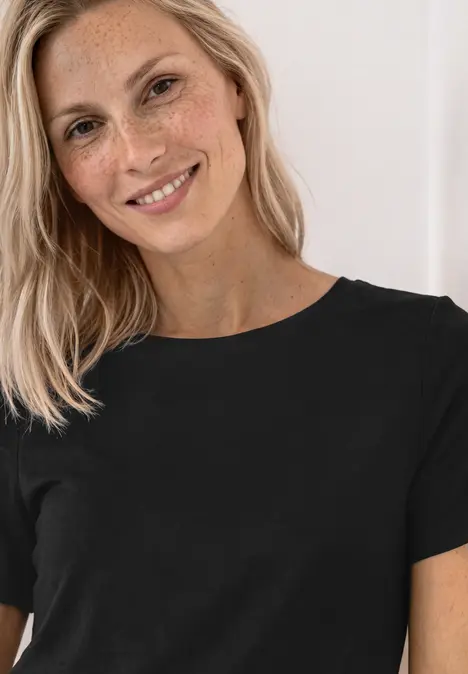 Eine lächelnde blonde Frau in einem schwarzen T-Shirt, vor hellem Hintergrund.