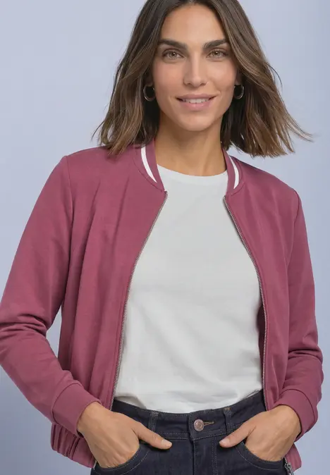 Frau mit pinker Bomberjacke, weißem T-Shirt und dunkler Hose, lässig posierend.