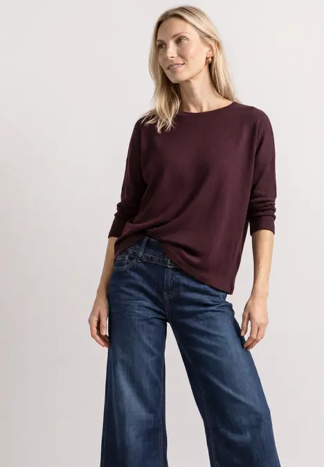 Frau trägt bordeauxroten Pullover und weite Jeans.