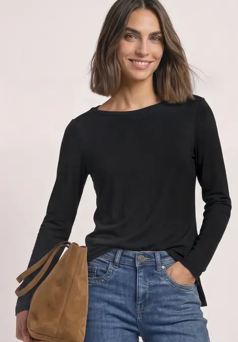 Frau in schwarzem Langarmshirt und Jeans mit brauner Tasche, lächelnd.