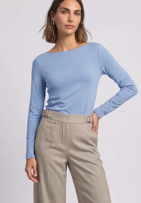 Frau in hellblauem Langarmshirt und beiger, hochtaillierter Hose mit Gürtelschnalle.