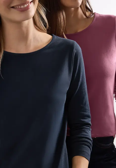 Deux femmes portent des hauts à manches longues, simples, un bleu marine et un bordeaux.