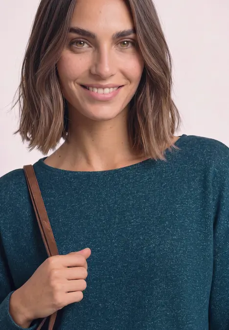 Een lachende vrouw met halflang haar in een glanzende blauwgroene top en een schoudertas