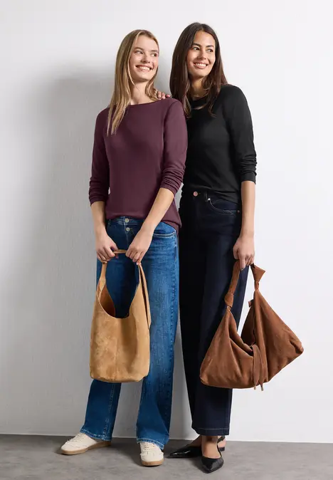 Deux femmes souriantes en jeans tiennent des sacs marron sur fond blanc.