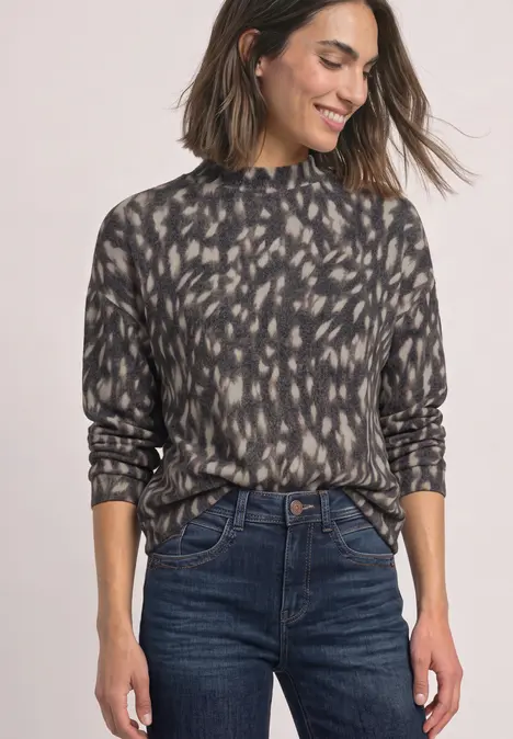Grau-schwarzer, abstrakt bedruckter Rollkragenpullover kombiniert mit dunklen High-Waist-Jeans.