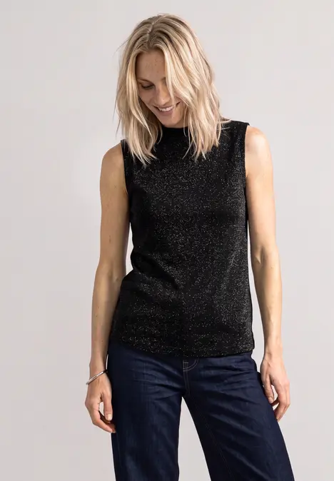 Eine Frau trägt ein schwarzes Glitzer-Top und blaue Jeans.