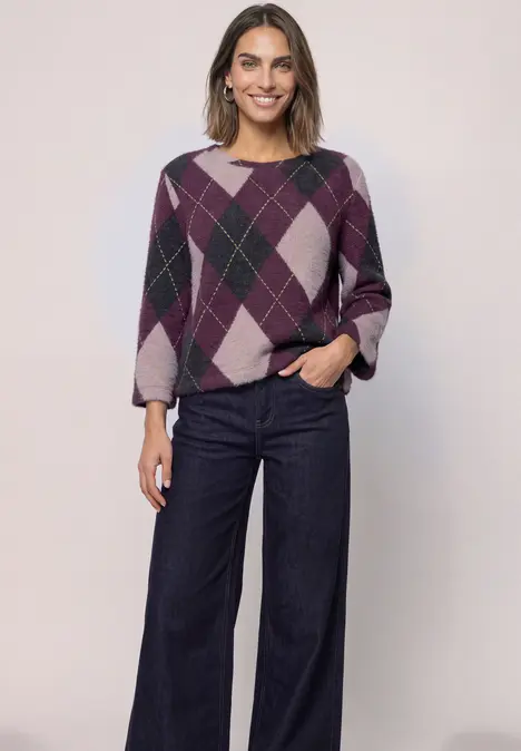 Eine Frau in lila Rautenmuster-Pullover und weiten Jeans.