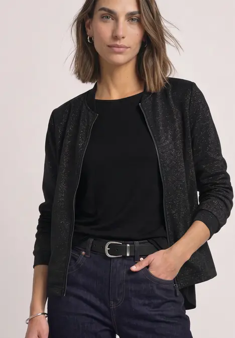 Eine Frau in schwarzem Top und strukturierter schwarzer Jacke mit Jeans und Gürtel, lässig gestylt.