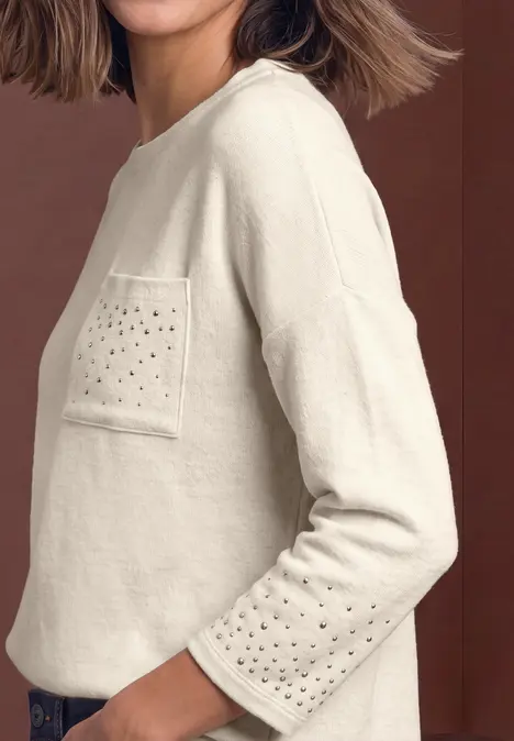 Beiger Pullover mit Brusttasche und Lochmuster auf Tasche und Ärmeln, seitliche Ansicht.