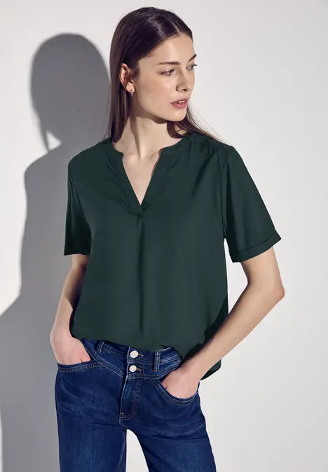 Frau mit dunkelgrünem Shirt und Jeans blickt seitlich.