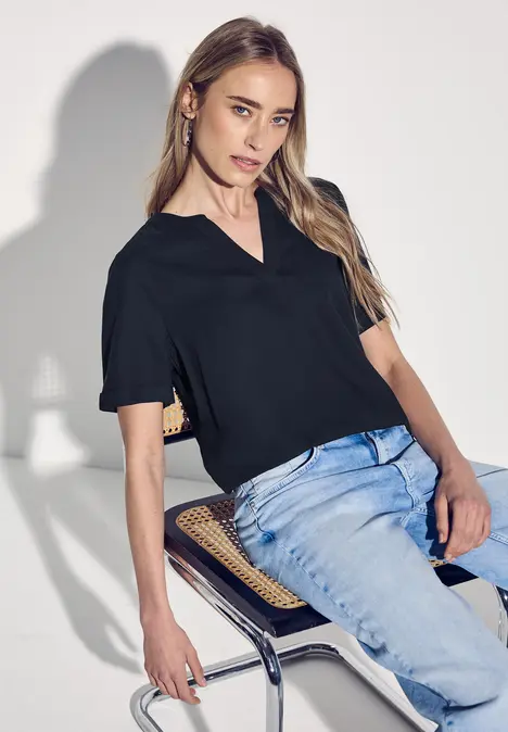 Frau mit schwarzem Shirt und Jeans sitzt auf einem Stuhl.