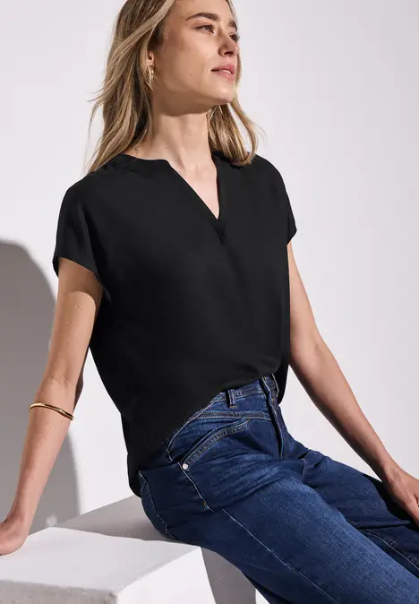 Frau mit schwarzem Oberteil und Jeans sitzt entspannt, schaut nach rechts.
