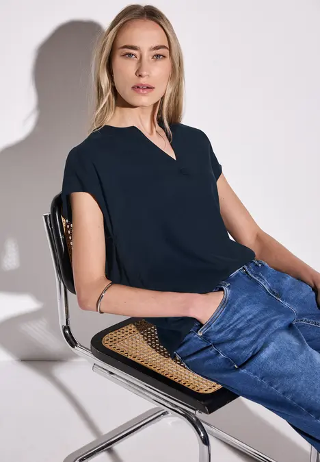 Frau sitzt entspannt auf einem Stuhl, trägt dunkelblaues Shirt und Jeans.