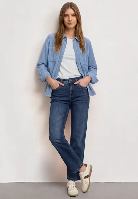 Frau trägt weißes T-Shirt, hellblaues Overshirt, dunkelblaue Jeans und helle Sneaker.
