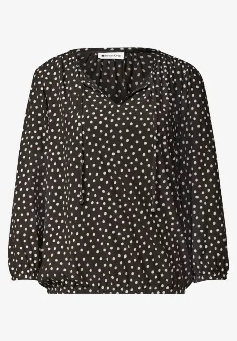 Schwarze Bluse mit weißem Herzpunkte-Muster, V-Ausschnitt und langen Ärmeln.
