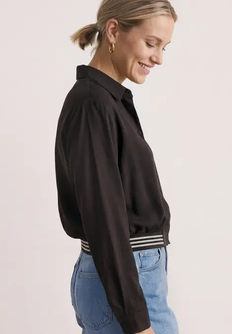 Seitlich abgebildete Frau mit schwarzer Bluse und Jeans, lächelnd.